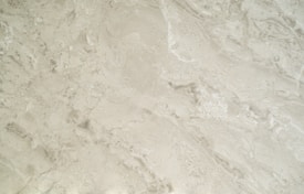 A close-up view of a smooth, creamy beige marble surface featuring intricate patterns and natural veining that give it a luxurious appearance.