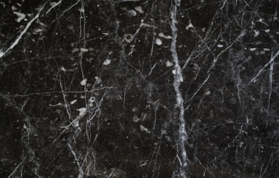 A dark marble surface characterized by intricate white veining and scattered white specks. The texture appears smooth and polished, common in natural stone countertops or flooring.