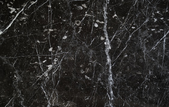 A dark marble surface characterized by intricate white veining and scattered white specks. The texture appears smooth and polished, common in natural stone countertops or flooring.