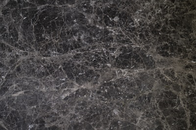 A detailed texture of dark marble with intricate white veining patterns running throughout the surface. The natural stone exhibits multiple shades of black and gray, creating an elegant and sophisticated appearance.