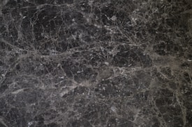 A detailed texture of dark marble with intricate white veining patterns running throughout the surface. The natural stone exhibits multiple shades of black and gray, creating an elegant and sophisticated appearance.