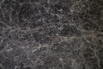 A detailed texture of dark marble with intricate white veining patterns running throughout the surface. The natural stone exhibits multiple shades of black and gray, creating an elegant and sophisticated appearance.