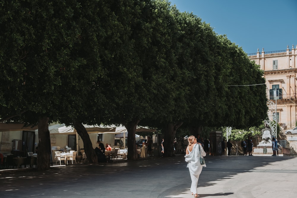 a woman walking down a street next to a tall tree