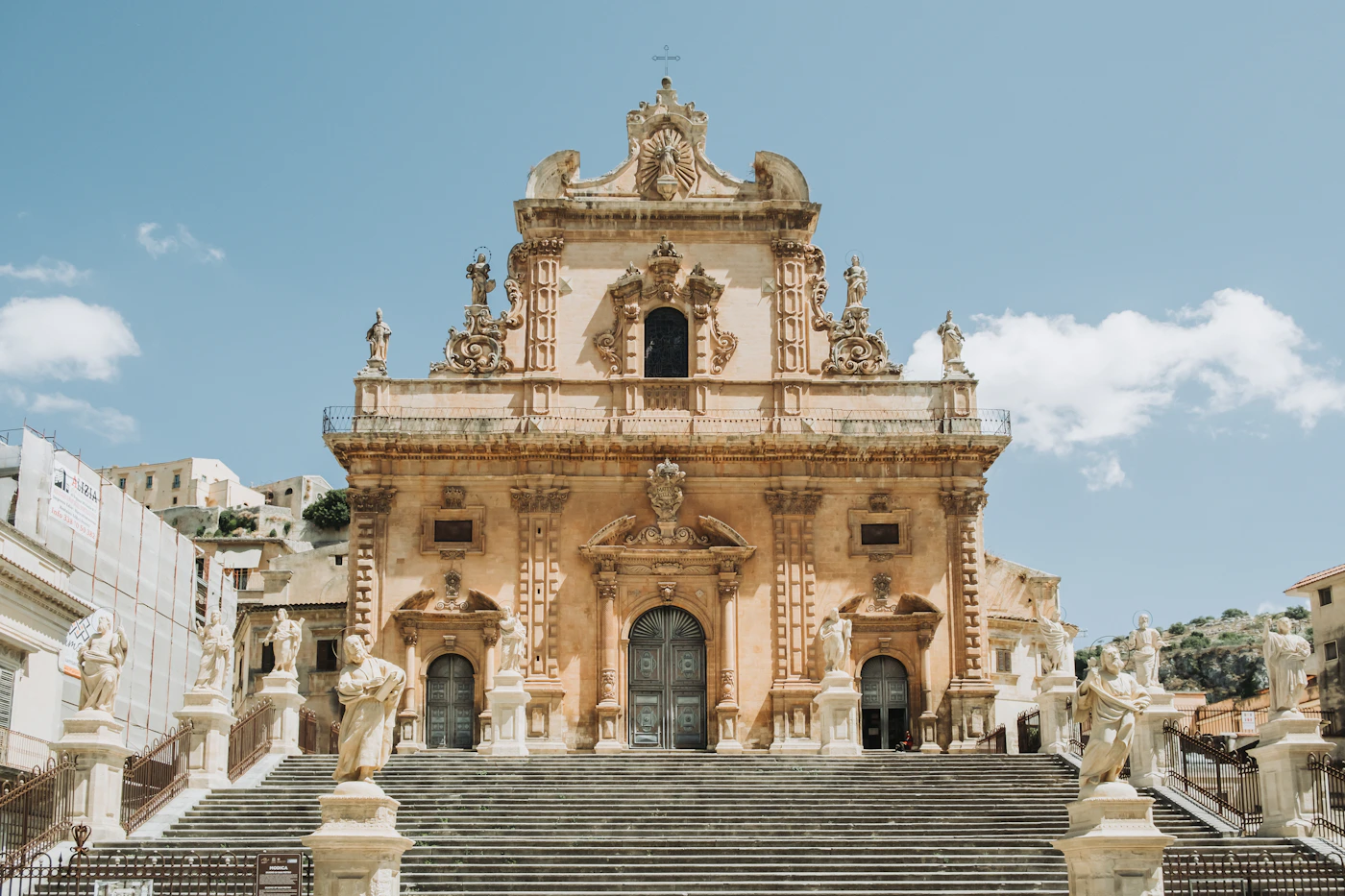 The grand baroque staircase of Modica cathedral in Sicily with ornate stone carvings golden facades and wide stone steps rising to the sky under bright Sicilian sunlight