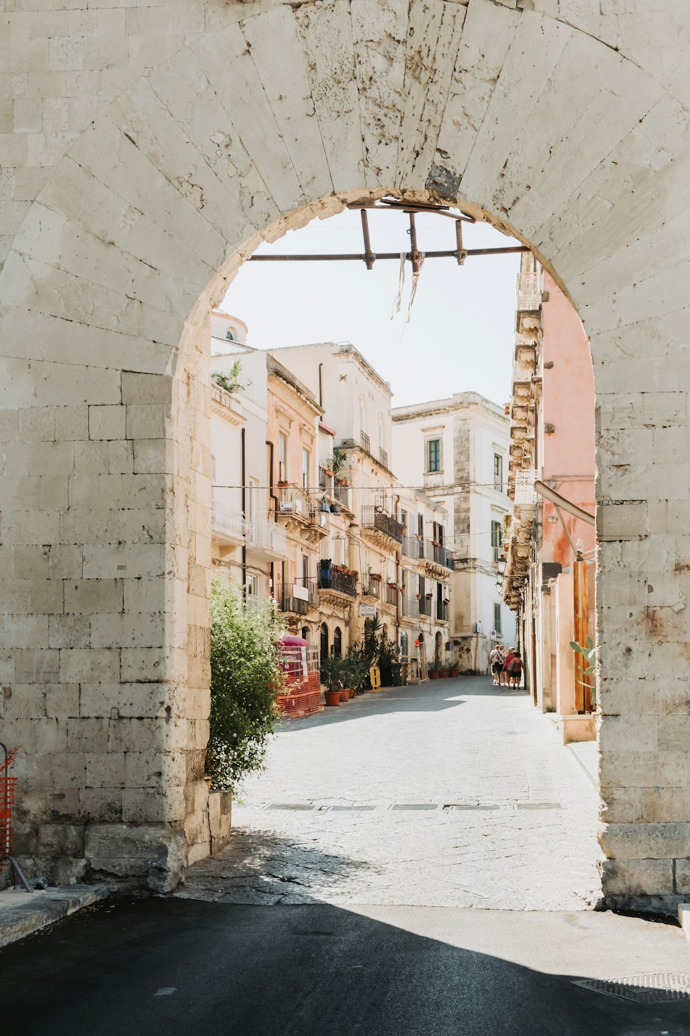 an arch in a stone wall leads into an empty street