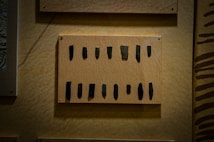A display of multiple small, dark, stone artifacts arranged in two rows on a wooden board mounted on a wall. The stones have varying shapes and appear to be carefully positioned, possibly for educational or exhibition purposes.