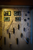 A museum exhibit showcasing ancient tools or artifacts mounted on a display board. Some items are enclosed in glass frames, while others are mounted directly onto the board. The backdrop includes illustrations or patterns that may resemble ancient maps or symbolic designs.