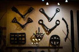 A display of various metal artifacts mounted on a wall, predominantly featuring tools or implements with intricate designs and geometric shapes. The items appear aged with a dark patina, suggesting historical significance.