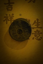 A round, ancient Chinese coin or medallion with detailed inscriptions, set against a golden background featuring Chinese characters.