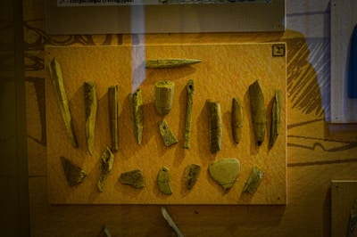A display of various ancient tools or artifacts made from bone or stone, mounted on a mustard-colored background, likely within a museum exhibit.