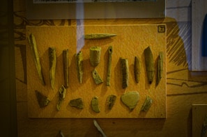 A display of various ancient tools or artifacts made from bone or stone, mounted on a mustard-colored background, likely within a museum exhibit.
