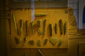 A display of various ancient tools or artifacts made from bone or stone, mounted on a mustard-colored background, likely within a museum exhibit.