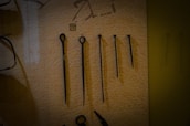 A set of five metal tools with a pointed end displayed vertically against a beige background. Each tool varies in length and design, with some featuring loops or rings at the top. There is a small numbered label '11' placed above the second tool from the left.