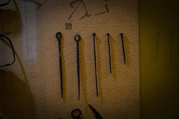 A set of five metal tools with a pointed end displayed vertically against a beige background. Each tool varies in length and design, with some featuring loops or rings at the top. There is a small numbered label '11' placed above the second tool from the left.
