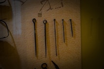 A set of five metal tools with a pointed end displayed vertically against a beige background. Each tool varies in length and design, with some featuring loops or rings at the top. There is a small numbered label '11' placed above the second tool from the left.