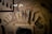 A collection of ancient artifacts displayed in a case. The items include various tools and ornaments arranged against a textured background with a faint image of an animal. Some of the items are numbered, such as a small comb and intricately carved handles or tools.