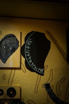 Various artifacts are displayed against a textured background. There is a large piece with inscriptions that appear to be runes or ancient script, alongside a metal plate with an embossed figure and further inscriptions. Other small components, including a pair of circular elements, are mounted around them.