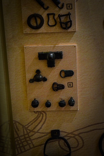 A display of various small, dark metal artifacts attached to a light background. The artifacts are arranged neatly on rectangular panels, numbered '4' and '6'. The objects vary in shape, including circles, loops, and more complex forms. The background has a subtle pattern.