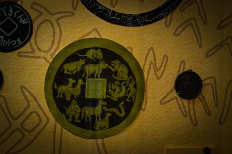 A detailed design featuring a circular motif with zodiac animal symbols surrounding a central square. The background is textured with abstract patterns and additional circular elements featuring intricate symbols.