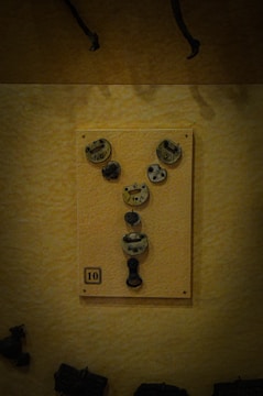 A collection of aged metal locks and keys displayed on a board with a numbered label '10'. The board is mounted on a textured yellow wall, and there are shadows implying a dim lighting setting.