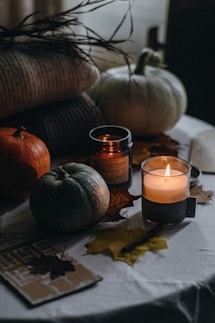 a table topped with a candle next to a pile of pumpkins