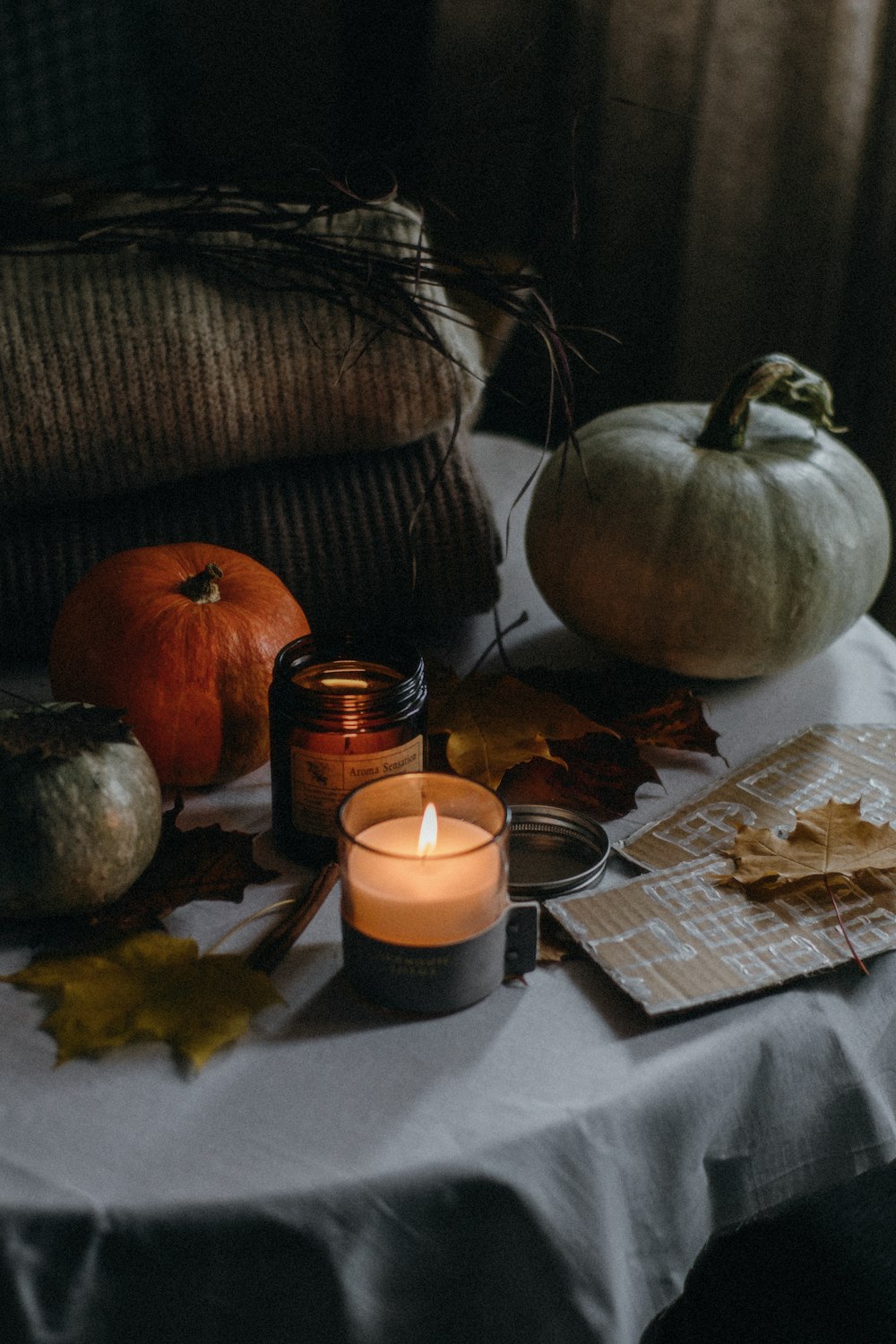 a table topped with a candle next to a pile of pumpkins