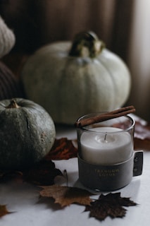 A collection of seasonal candles with autumn leaves and cinnamon sticks arranged around them.