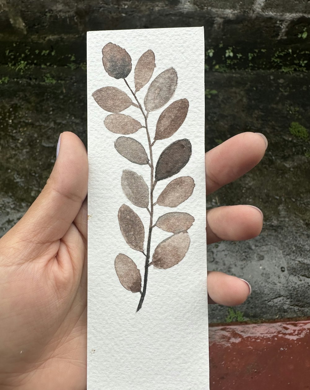 a hand holding a piece of paper with a painting of a leaf on it