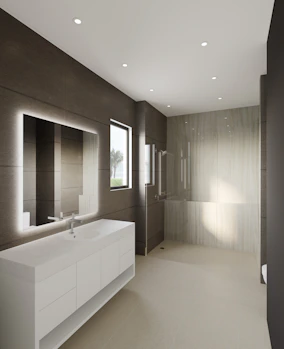 A bathroom with white tiles, a frameless mirror, and simple fixtures emphasizing elegance and function.