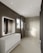 A modern bathroom features large, smooth tiles on the walls and floors, a sleek white countertop with built-in sink and storage cabinets, and a large illuminated mirror. Recessed ceiling lights provide ample illumination, and a walk-in shower with a glass partition is situated at the far end. A window allows natural light to enter, enhancing the minimalist aesthetic.