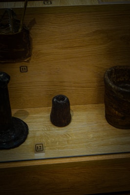 Several dark, ancient-looking objects are displayed on a wooden platform. Each item is labeled with numbers, suggesting a museum or exhibit setting. The objects vary in shape and size, including a small conical piece in the center.