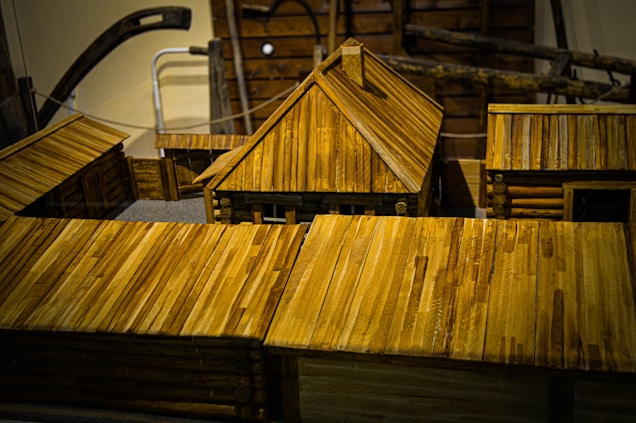 Wooden model buildings featuring log cabin construction and prominent plank roofs dominate the scene. The craftsmanship displays detailed joints and fittings that reflect traditional architecture. The structures are arranged in a way that suggests a small village or settlement.