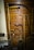 A collection of vintage wooden farming tools hangs on a wooden wall. The tools include sickles, a rake with wooden handles, and other implements. The wood shows signs of age and use, giving a rustic, historical texture.