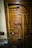 A collection of vintage wooden farming tools hangs on a wooden wall. The tools include sickles, a rake with wooden handles, and other implements. The wood shows signs of age and use, giving a rustic, historical texture.