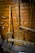 A variety of old wooden tools are displayed against a wooden wall. The tools include large paddles and wooden handles, possibly used for agricultural or manual tasks. The wood has a weathered look, indicating age and use.