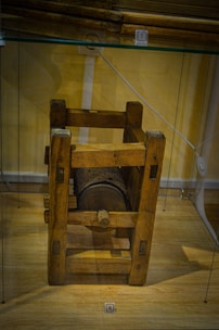 A wooden medieval-style mechanism displayed in a glass case; it features a cylindrical drum with perforated metal grating and sturdy wooden supports.