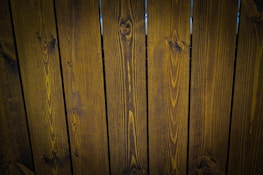A close-up view of vertically arranged wooden planks with visible grain patterns and a dark brown stain.