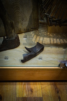 A museum exhibit displaying a collection of ancient tools or artifacts. The central focus is a wooden or metal implement placed on a wooden floor within a transparent case, with small numbered labels nearby.