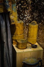A display of intricately designed wooden containers and a fabric drape. The containers have detailed carvings and patterns, showcasing expert craftsmanship. The drape features a decorative design with blue and brown tones. The background has a textured appearance.