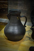 A copper pitcher with intricate detailing sitting on a wooden surface.