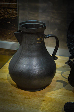 A copper pitcher with intricate detailing sitting on a wooden surface.