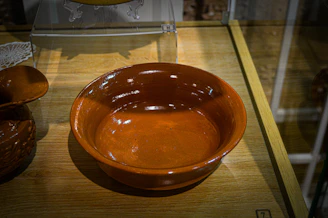 Close-up of a handcrafted ceramic bowl with warm red and blue glaze tones on a simple white background.