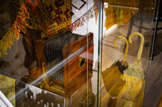 An antique wooden camera with bellows is displayed in a glass case alongside an intricately patterned textile with warm colors. Nearby, a collection of vintage umbrellas with curved handles is arranged, creating a sense of nostalgia.