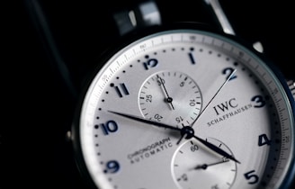 A close-up view of a stylish wristwatch featuring a white dial with black numerals and two subdials. The watch is branded with 'IWC Schaffhausen' and includes the words 'Chronograph Automatic'. The hands are sleek and contrast sharply against the dial, which has a silver finish adding to the elegance of the design.