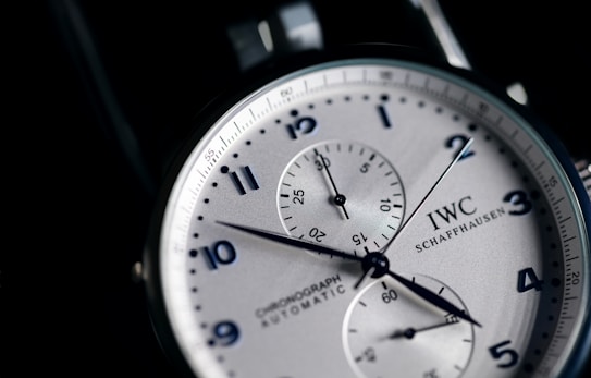 A close-up view of a stylish wristwatch featuring a white dial with black numerals and two subdials. The watch is branded with 'IWC Schaffhausen' and includes the words 'Chronograph Automatic'. The hands are sleek and contrast sharply against the dial, which has a silver finish adding to the elegance of the design.