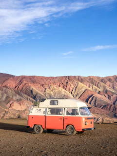 A rugged van parked at golden hour against a backdrop of towering desert cliffs and clear blue sky.