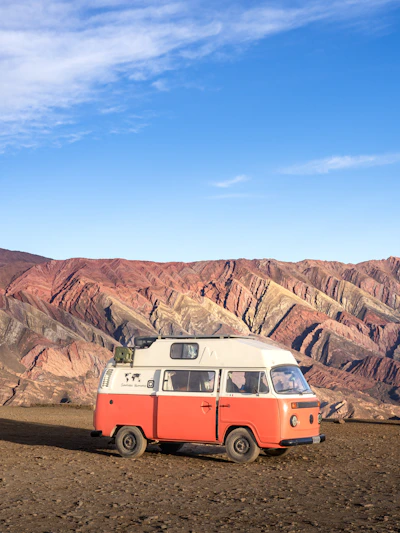A rugged van parked at golden hour against a backdrop of towering desert cliffs and clear blue sky.