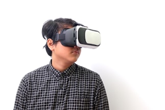 A person wearing a virtual reality headset, gazing off to the side, dressed in a black and white checkered shirt, against a plain white background.