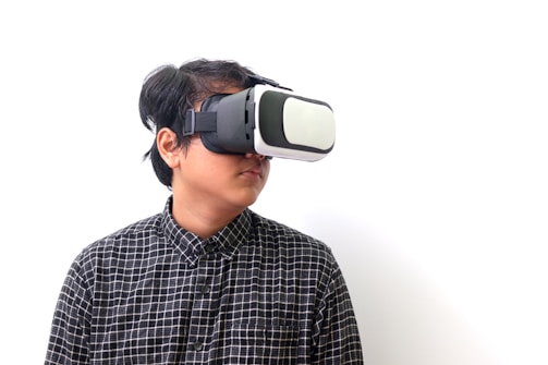 A person wearing a virtual reality headset, gazing off to the side, dressed in a black and white checkered shirt, against a plain white background.