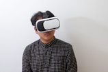 A person wearing a black and white plaid shirt uses a virtual reality headset against a plain white background.